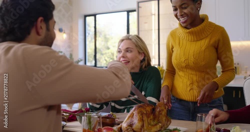 Diverse friends carving turkey at home as host placing platter, knife, pouring sauce