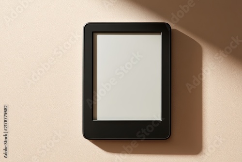 E-reader tablet showing blank screen on beige background with natural shadow