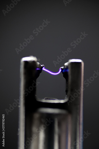 Detailed macro shot of a glowing purple plasma arc discharging between two lighter electrodes.