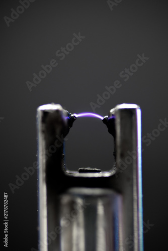 Detailed macro shot of a glowing purple plasma arc discharging between two lighter electrodes.