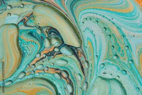 Abstract macro liquid background with turquoise and orange swirled paint covered in oil bubbles.