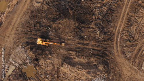 Aerial view of an excavator working on a muddy construction site with deep tire tracks and disturbed earth in India.