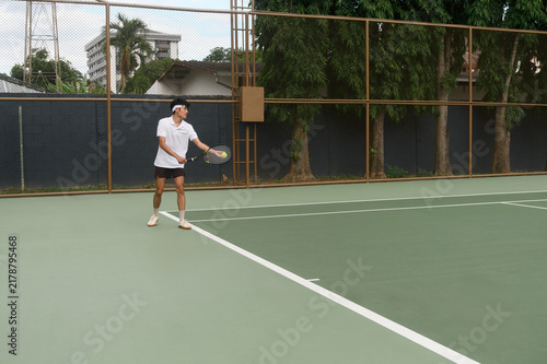 Принти на полотні Young Asian Man Playing Tennis on Outdoor Green Court, Hitting Backhand Shot wit