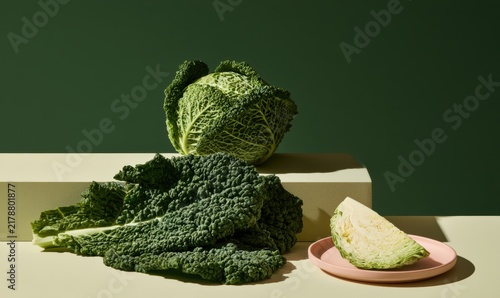 Organic green cabbage, sliced piece, and loose leaves on styled surface