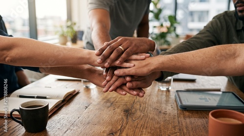 Diverse business colleagues stacking hands together over a wooden meeting table to symbolize unity partnership cooperation and professional team synergy