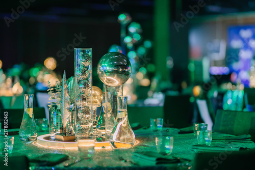 Elegant dining table centerpiece featuring glass vases, decorative elements, and illuminated spheres in a sophisticated event setting with green lighting