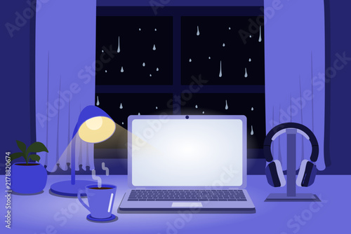 Cozy rainy night home office with laptop, headphones, coffee and desk lamp