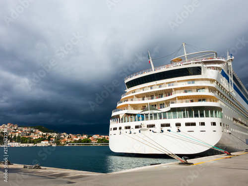 White cruise ship moored in the Port of Dubrovnik, Gruz, Croatia under dramatic storm clouds over the Adriatic Sea.