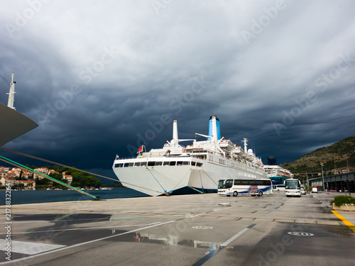 Cruise ship during passenger embarkation, docked in Port of Dubrovnik Gruz, Croatia, under dramatic storm clouds, Adriatic sea.
