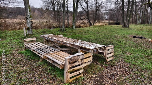 Obraz na plátně On the grassy riverbank, strewn with fallen leaves, there is a table and benches made of wooden pallets