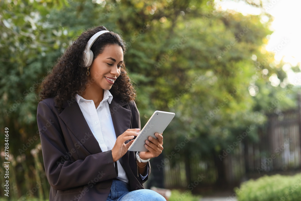 Fototapeta premium Remote work and digital nomad lifestyle, young woman using tablet with headphones in park for freelance business communication and online education