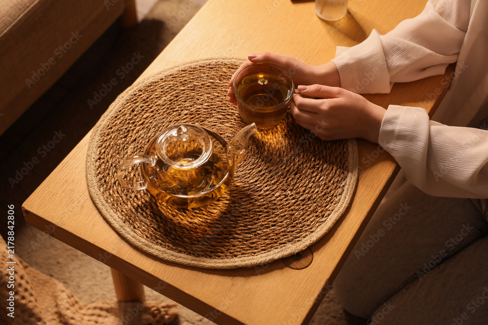 Fototapeta premium Mindfulness and self care, woman drinking herbal tea at home for relaxation and stress relief in a cozy living room setting with warm evening light