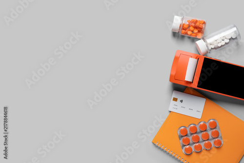 Payment terminal with credit card, notebook and pills on light background