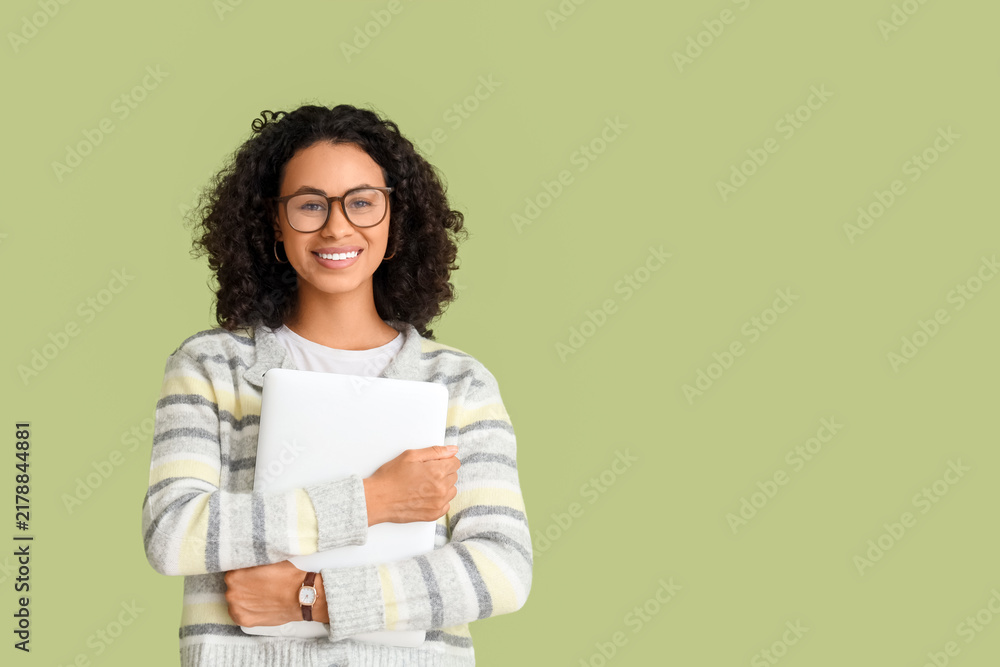 Fototapeta premium Young African-American woman with laptop on green background