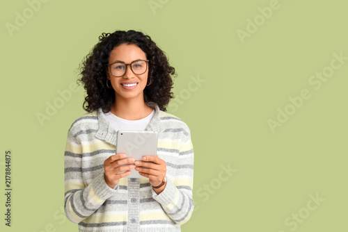 Young African-American woman with tablet computer on green background