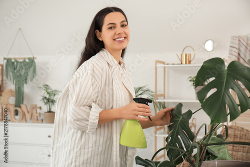 Young woman spraying houseplants in stylish room
