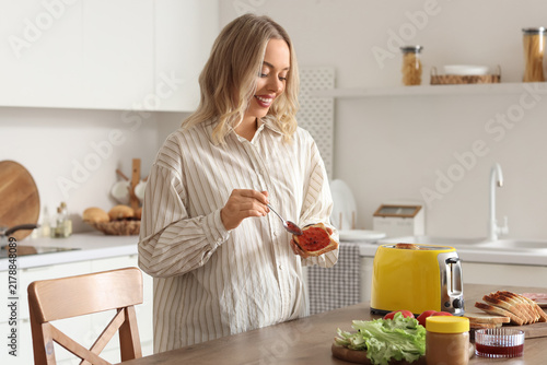Young beautiful happy woman making tasty toasts with jam in kitchen