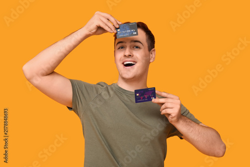 Young man with credit cards on yellow background
