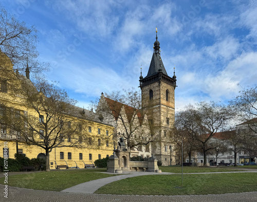 serene historical tower standing in urban park with stone and metal materials and yellow and brown colors in foreground view, featuring benches and trees for a peaceful setting.
