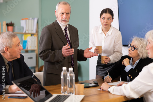 Foto Irritated elderly male boss reprimanding upset subordinates sitting at table in