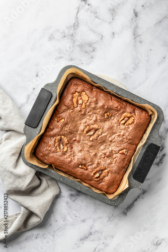 Chocolate brownie in baking form on white marble background top view. Process of making chocolate brownie. Home baking culinary concept, recipe