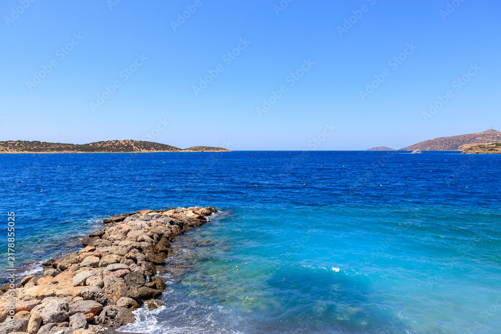 Fototapeta premium Calm blue sea meets rocky shore under clear sky