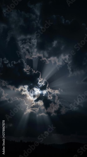 Bright full moon shining through moving dark storm clouds at night. Eerie atmospheric mood with dramatic glowing light rays. Halloween 2026 spooky night background theme concept.