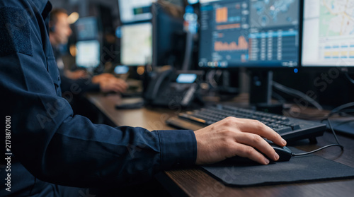 Dispatcher sit at desks working on computers using mouse and keyboard. Male 911 worker in uniform working at multi monitor dispatch station