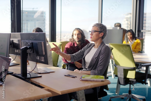 Fotografía Confident mature businesswoman pointing at a monitor while explaining information to colleagues in a bright open office