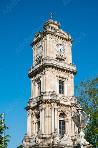 Clock tower with ornate design and white fence in sunny park setting