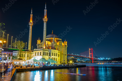 Night view of grand mosque beside river with illuminated bridge in background