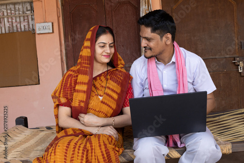 Photography Indian happy young rural couple working on laptop while sitting on traditional b
