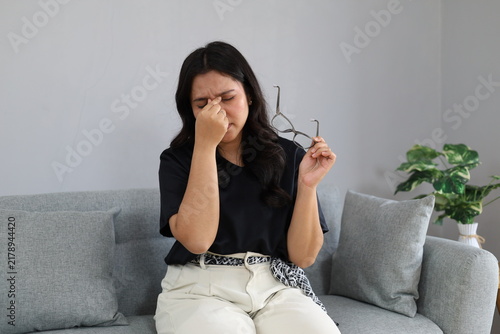 Принти на полотні A young woman sat on the sofa in her home, removed her glasses, and rubbed her eyes from exhaustion