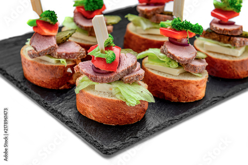 Tasty bite-sized sandwiches with meat and vegetables on a black tray. Small sandwiches made with bread, meat, lettuce, and vegetables served on a black tray at a gathering.