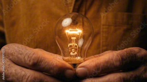 A close-up shot of hands holding a glowing incandescent light bulb, representing an idea or innovation
