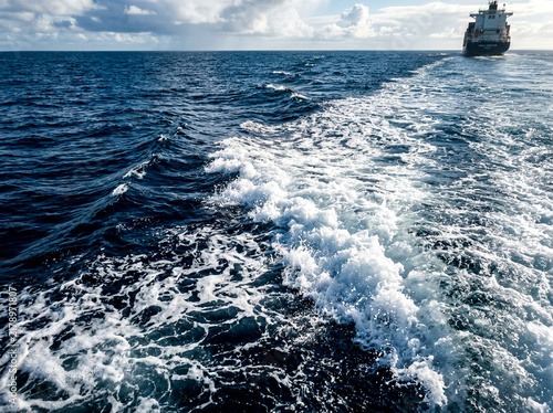 Cargo ship sailing on deep blue ocean with white water wake trail in open sea