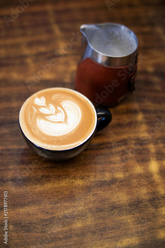 Cuadro en lienzo A freshly prepared cup of latte art placed beside a stainless steel milk pitcher on a wooden table