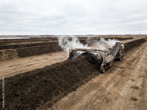 Obraz na płótnie Industrial compost turner processing steaming organic matter in long dark windrows