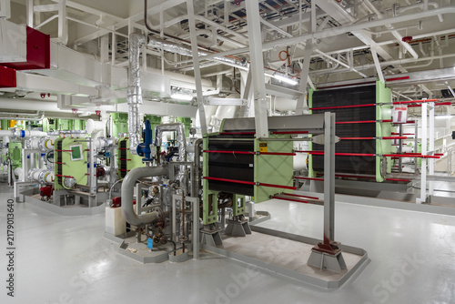 Foto View from a platform inside the engine room of a modern commercial vessel, showing several cooling water heat exchangers serving the main engine and auxiliary shipboard systems