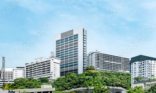 Contemporary building complex rising above dense green vegetation in Hong Kong, with clean architecture and blue sky suggesting healthcare, sustainability and urban development.