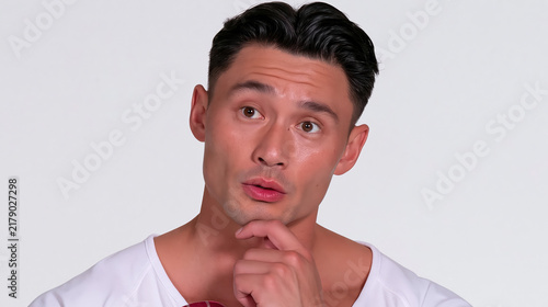 Asian man showing mildly confused expression with hand on chin against plain studio background