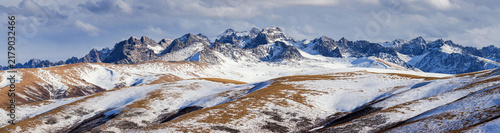 Cuadro en lienzo A panoramic view of snow-covered mountain ranges and rolling alpine terrain under a partly cloudy sky, showcasing pristine natural scenery