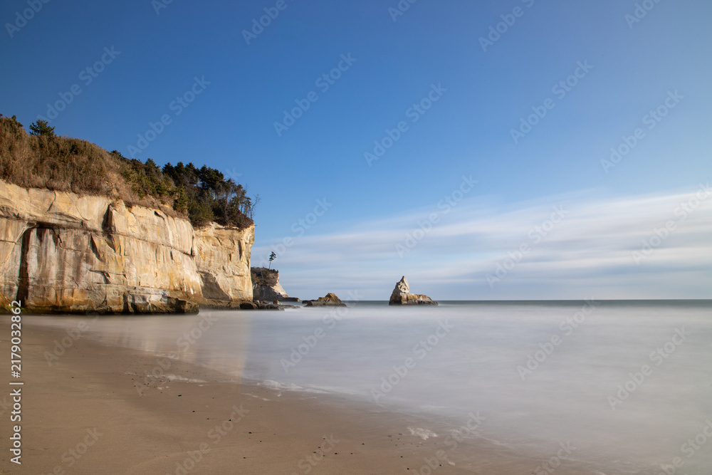 Fototapeta premium Scenic Coastal Cliff and Calm Sandy Beach Under Blue Sky