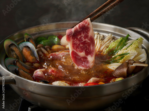 Steaming bowl of gourmet Asian hotpot featuring raw beef, mushrooms, and fresh vegetables simmering in savory broth