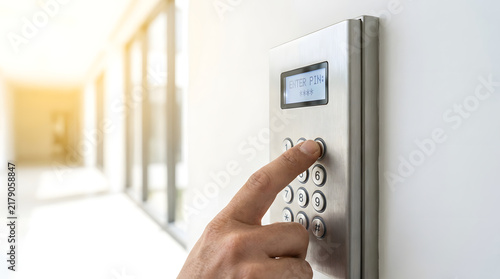 Hand entering secure PIN code on a modern metal keypad in a bright office hallway for access control and building security.