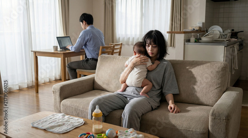 Fototapeta 在宅勤務をする夫の背後で育児に疲れ果てて呆然とする母親