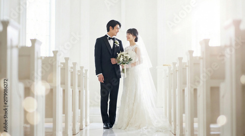 Fototapeta 白いチャペルのバージンロードに立ち笑顔で見つめ合う日本人新郎新婦の全身