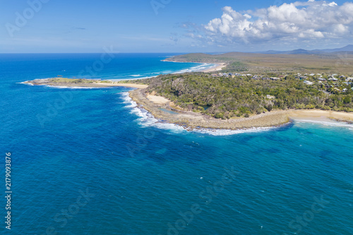 Aerial view of Spooky Beach and the rugged rocky coastline extending towards Angourie Point, with coastal vegetation and the town of Angourie visible in the background on the NSW North Coast