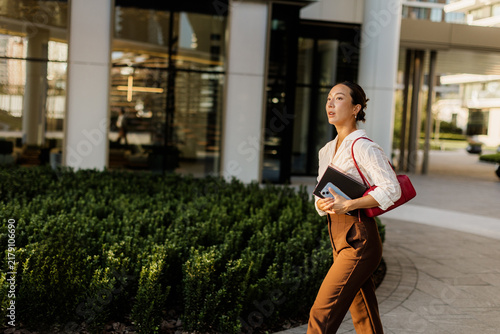Korean woman in formal attire walks confidently through a modern urban setting