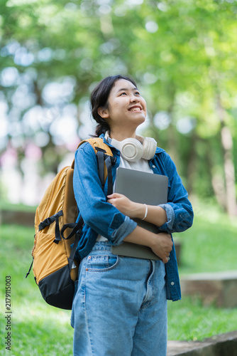 Happy student standing outdoors holding laptop looking up
